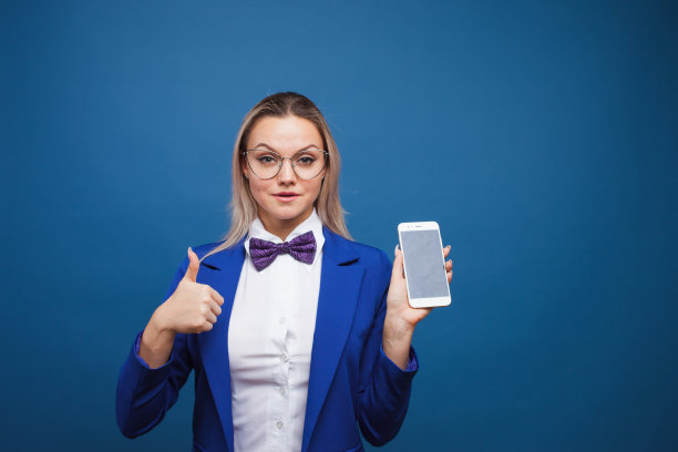 可爱又有趣的女商人穿着时尚的蓝色夹克，打着领结，用的是智能手机。图片下载