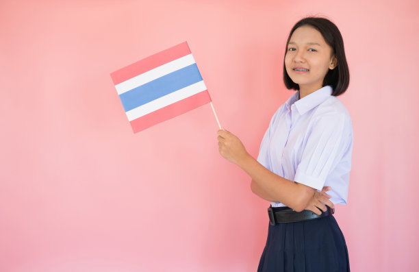 肖像亚洲年轻女孩持有泰国国旗与粉红色的背景在学生制服。图片下载