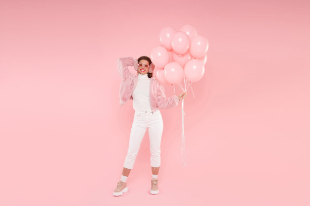完整的长肖像年轻的少女戴着手臂轰炸机，耳朵保暖器和眼镜，为派对举行生日气球，孤立在粉红色的背景图片下载