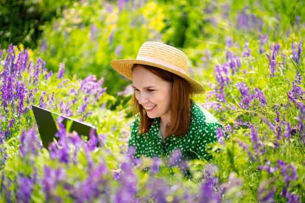 一名女子在花丛中用笔记本电脑工作。农村移动互联网建设。图片下载