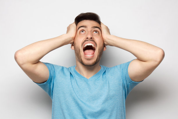 年轻人一边抬头大叫，一边受到噪音的压力，双手紧闭耳朵，孤立在灰色背景中图片下载