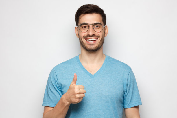 身穿蓝色t恤的年轻人在灰色背景上孤立地竖起大拇指图片下载