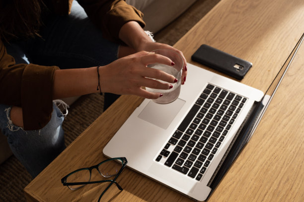 女孩坐在家里，手上拿着一杯水，看着笔记本电脑的屏幕。家庭工作空间-在家工作的概念和生活方式图片下载