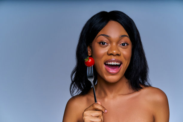 特写快乐的女人大声与叉子与一个红色的西红柿刺在她的脸。饮食概念图片下载