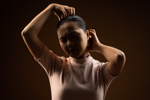 亚洲女人抓着头，孤立地站在米色背景上。图片下载