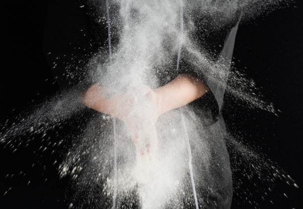 在黑暗的背景上，面包师的手筛着白面粉图片下载