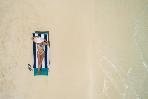 在马尔代夫，苗条的女人躺在沙滩椅上晒太阳的鸟瞰图。夏天的海景有女孩，美丽的海浪，五颜六色的水。无人机俯视图。图片下载
