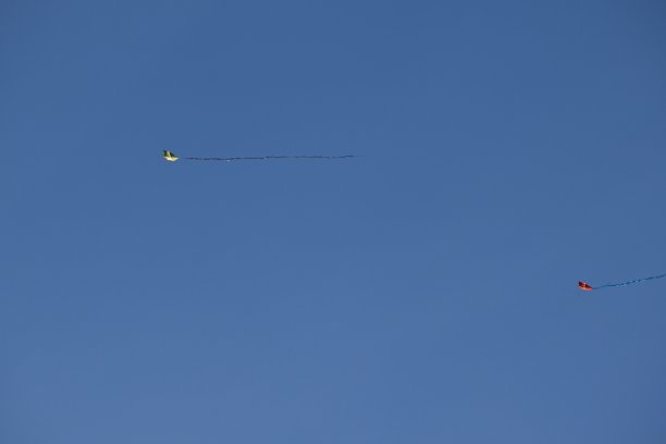 在万里无云的蓝天下，两只彩色纸风筝平行地漂浮着。图片下载