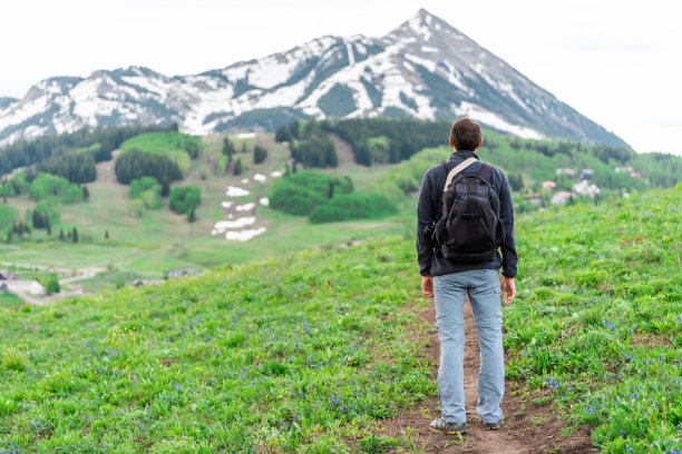 一名男子站在斯诺德格拉斯小径上，以散景为背景，观看夏季的峰丘、科罗拉多峰和村庄图片下载
