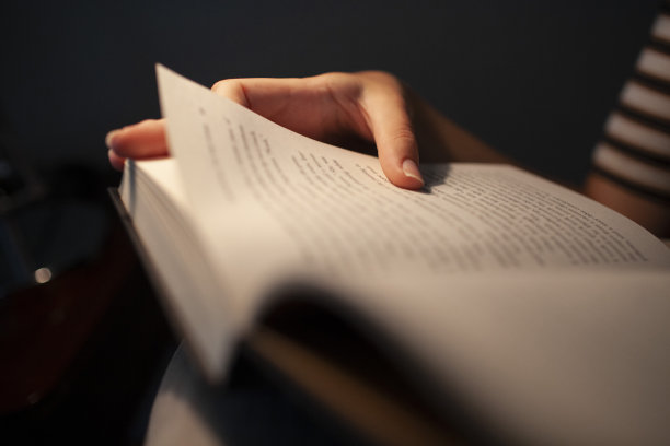 在昏暗的光线下拿着一本书的手的特写图片下载