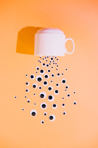 从一个倒置的白色杯子或马克杯中，卡通玩具的眼睛溢出或散落在一个色彩柔和的超现实主义黄色背景上。图片下载