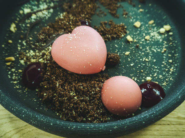 这张特写照片是一个绿松石盘子的碎片，上面有一个粉红色的心形甜点和一个装在饼干屑里的圆球。聚焦在中心。模糊的背景图片下载