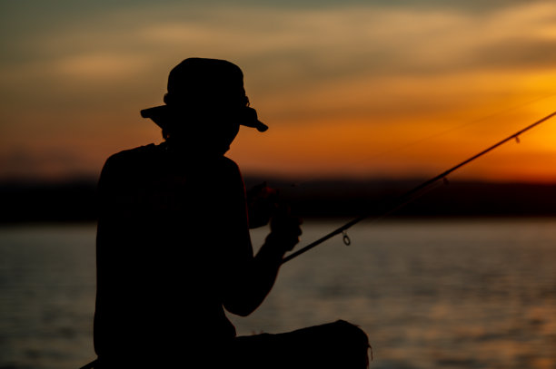 在剪影日落的时候，渔民们在水库里用钓竿钓鱼。图片下载