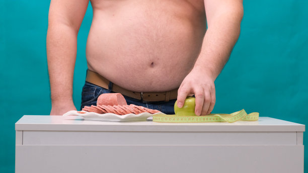 一个大肚子的男人在香肠和青苹果之间选择。饮食和意志力的概念图片下载