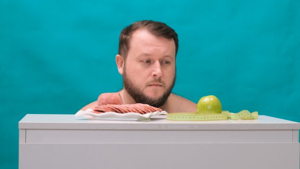 长胡子的胖子在绿屏幕上选择香肠还是青苹果。抵制诱惑，快餐，健康饮食，饮食，身体保养图片下载