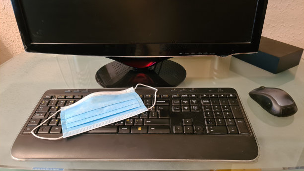 蓝色医用口罩放置在办公室玻璃桌上的键盘上图片下载