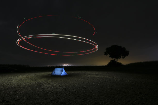 晚上在户外照片。草地上有一个帐篷，无人机在上面盘旋。长快门速度的照片含有颗粒。用无人机进行光绘。图片下载