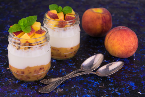 用薄荷叶装饰的罐子里的桃子酸奶在蓝色的背景上。图片下载