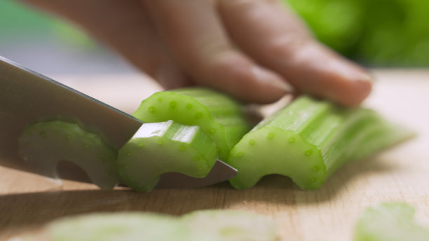 一个女人在厨房里准备食物，她正在切菜板上用一把刀切新鲜芹菜图片下载