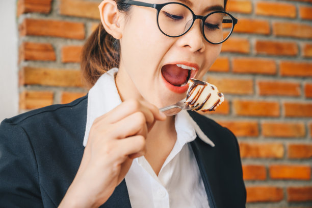 肖像年轻的亚洲妇女打开她的嘴吃一块可丽饼。图片下载