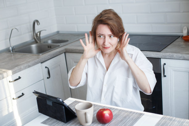 在隔离禁闭的厨房里穿着白衬衫用笔记本电脑喝咖啡或茶的女人。拿着平板电脑的女孩图片下载