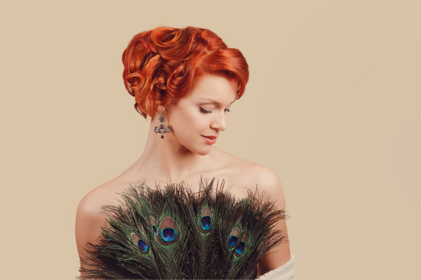 特写红头发美丽的年轻女子快乐的海报女郎穿着孔雀羽毛制成的衣服，与卷曲的发髻复古的发型图片下载