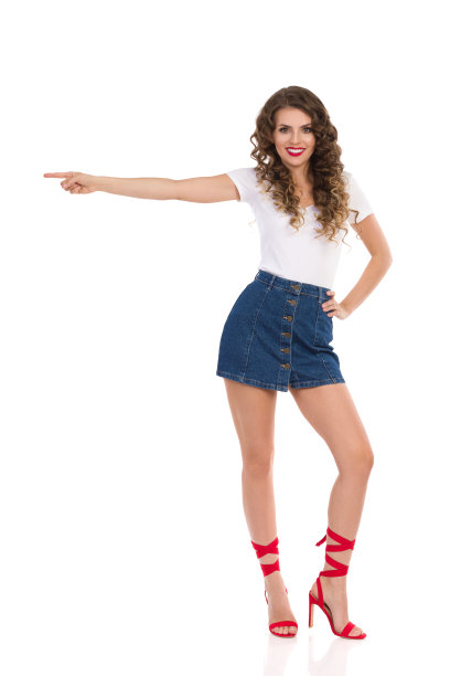 微笑的年轻女子在牛仔裤迷你裙和红色高跟鞋是指着一边。图片下载