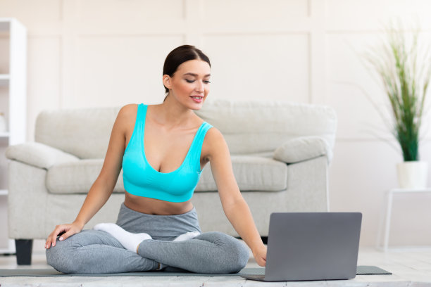 女孩坐在室内垫子上用笔记本准备做瑜伽图片下载