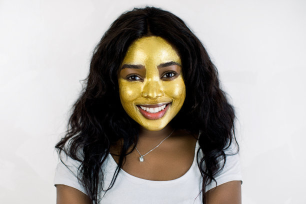 特写美丽迷人的非洲年轻女孩与健康柔软的皮肤，抗老化黄金化妆品面膜，看着相机，而站在孤立的白色背景图片下载