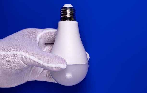 手拿一只白色手套与一个二极管放在蓝色的灯上。图片下载
