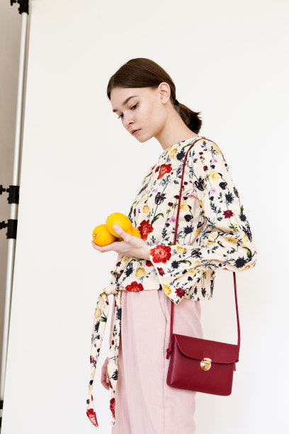 美丽的年轻女子与裸色化妆穿衬衫印花和粉红色的裤子拿着水果在白色的背景图片下载