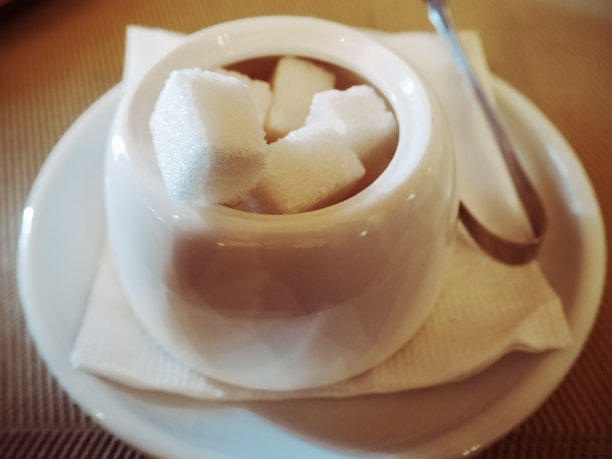 一个白色杯子的特写照片，糖和钳子站在一个碟子上。效果很模糊。照片与过滤器图片下载