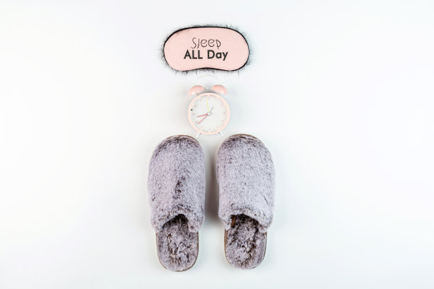 平躺着柔软的毛绒拖鞋灰色，眼罩和粉色闹钟隔离在白色的背景。顶视图，开销，模型，模板，复制空间。时间休息图片下载