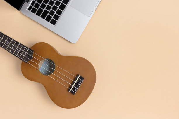 笔记本电脑和四弦琴在米色背景和文字的地方。图片下载