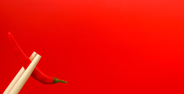 用木筷子夹着红色背景上的一荚红辣椒。刺激的概念。自由空间图片下载