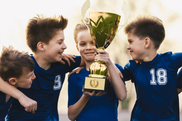 快乐的孩子在运动队庆祝成功的学校比赛。年轻的白人男孩拿着金杯。少年足球队赢得少年比赛素材图片