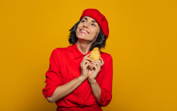 是我的荣幸!这是一名年轻游客的半长照片，她穿着巴黎风格的衣服，戴着红色贝雷帽，看起来就像在天空中一样梦幻，因为她手里拿着一块法国糕点。图片下载