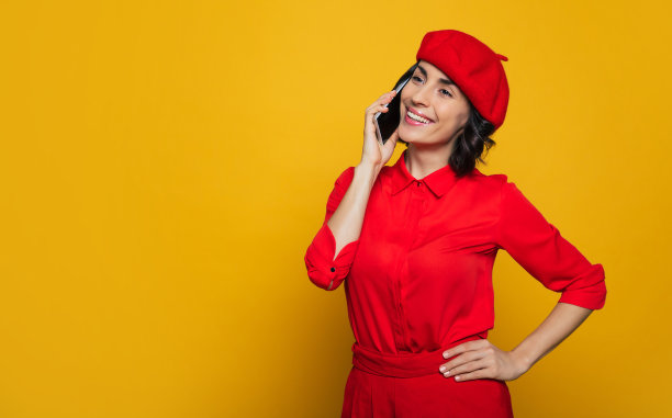 你好，我在旅行中。一个迷人的法国女人的半长照片，戴着红色贝雷帽，享受她的旅程和打电话。图片下载