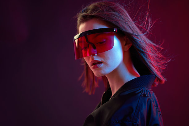 一个很酷的女孩的肖像，穿着黑色短夹克，戴着墨镜，背景是霓虹灯。图片下载