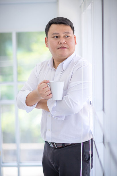 自信地望向窗外，手持咖啡杯的亚洲男士图片下载