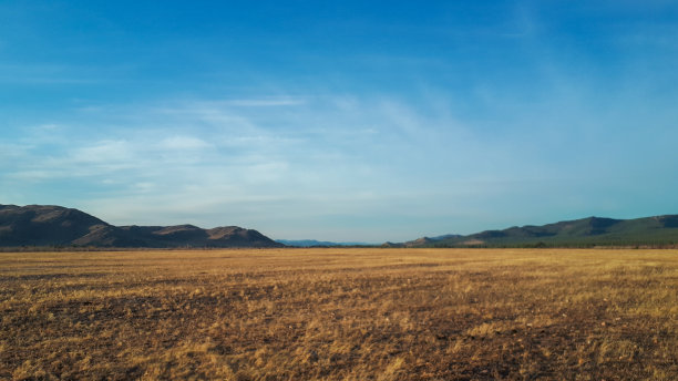 照片中的草原农地牧场在日落与明亮的蓝天白云在春天的中间，以山和山覆盖着松树林的背景图片下载