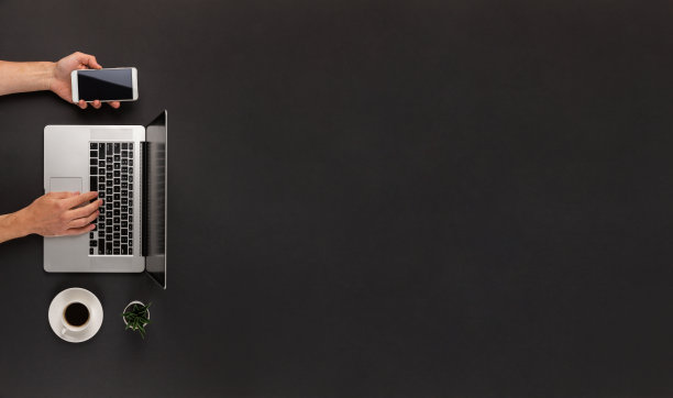 男性双手在笔记本电脑上打字，同时使用智能手机，在抽象的暗黑色办公桌上，有巨大的拷贝空间图片下载