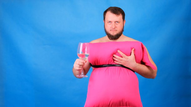 一个滑稽的留着胡子的家伙，穿着粉红色的枕头做的裙子，在蓝色的背景上触摸着他的胸部。疯狂的检疫。有趣的打扫屋子。2020年时尚。放在枕头上。由于房屋隔离，挑战2020图片下载