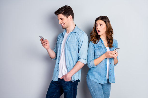 照片相当有趣的女士看电话帅哥可疑的女朋友认为男朋友欺骗她穿休闲牛仔衬衫装孤立的灰色背景图片下载