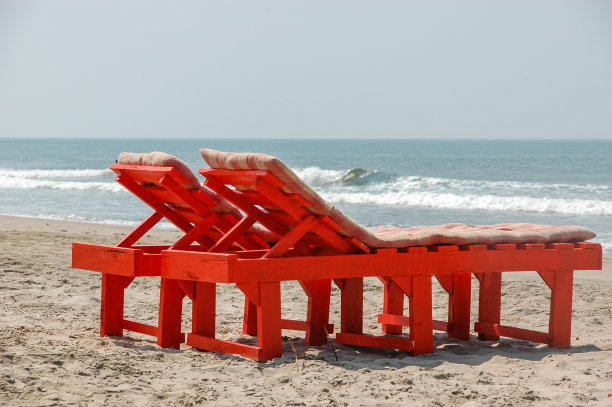 海边有两张木制的红色日光浴床。度假度假旅游的背景概念图片下载