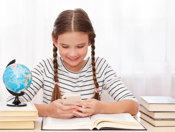 教育和办学理念。孩子正坐在桌子旁，使用手机图片下载