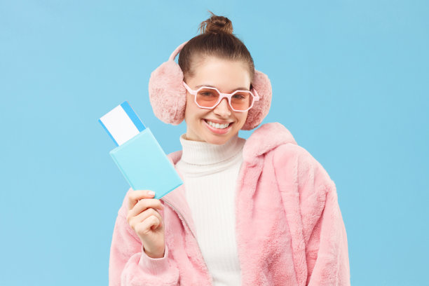 年轻的女游客拿着护照和机票，等待旅行，孤立在蓝色背景。冬季旅游与旅游理念图片下载