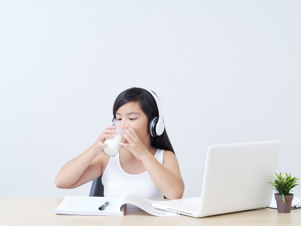 小女孩在家边喝牛奶边用笔记本电脑在线学习。图片下载