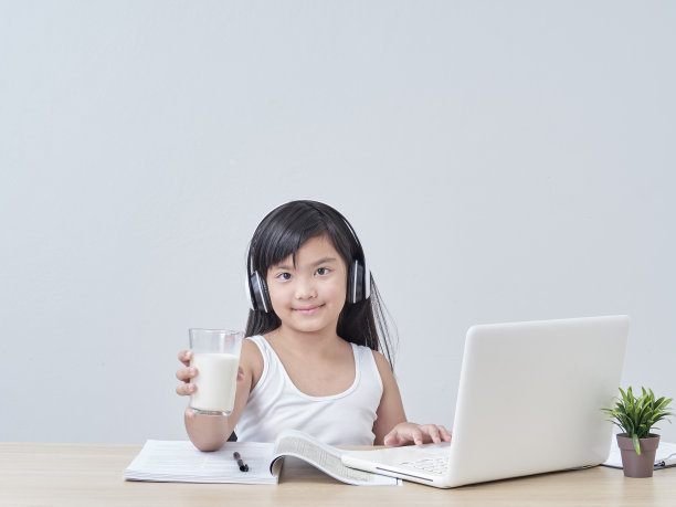 小女孩在家里用笔记本电脑上网学习，喝着牛奶。图片下载