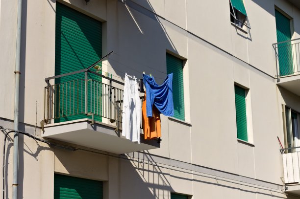 衣服挂在带有绿色百叶窗的房子阳台外的一根电线上(意大利，欧洲)图片下载